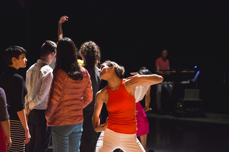 A woman in a bright orange halter strikes a pose as audience members filter in